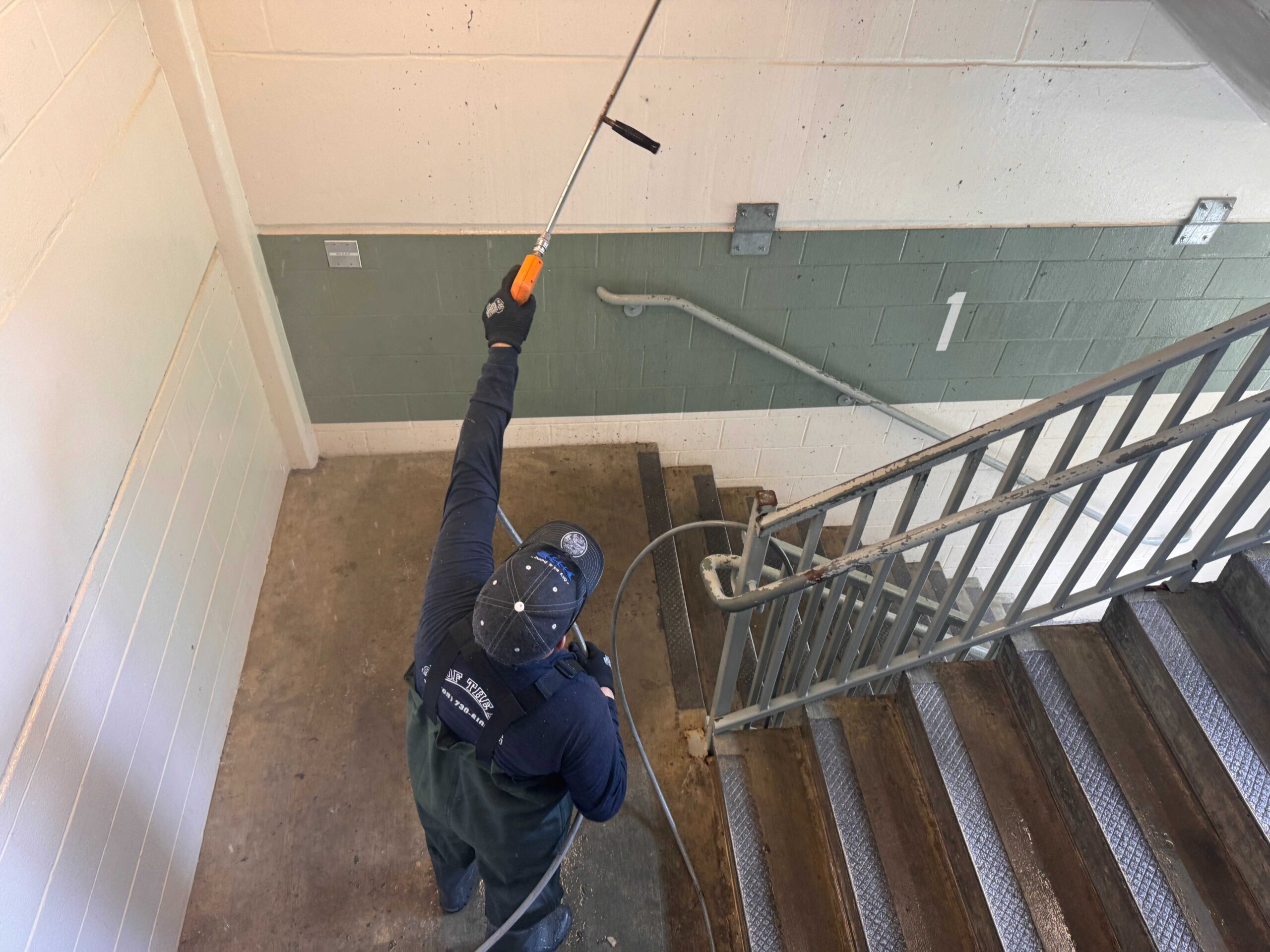 Technician pressure washing a stairwell and handrail at a commercial parking structure