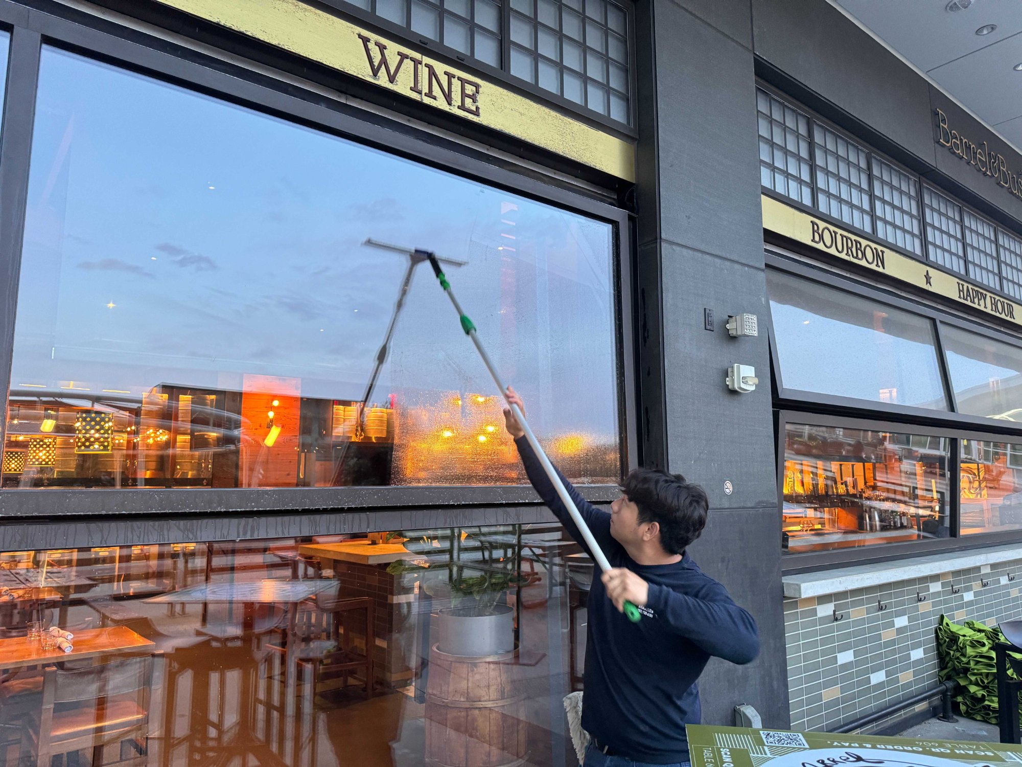 Technician using a squeegee to clean storefront glass at a restaurant entrance
