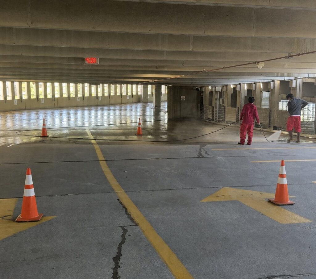 Top of the Line crew pressure washing a parking garage with safety cones marking the work area.