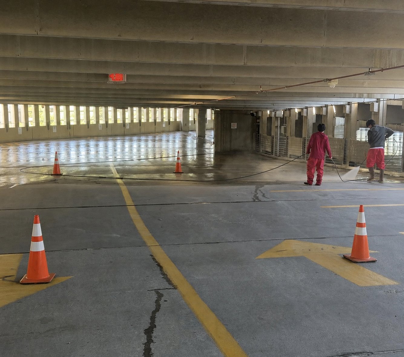 Top of the Line crew pressure washing a parking garage with safety cones marking the work area.