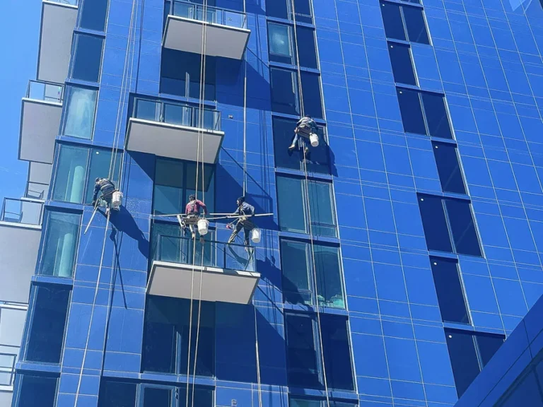 Multiple rope-access technicians cleaning windows and balconies on a high-rise building