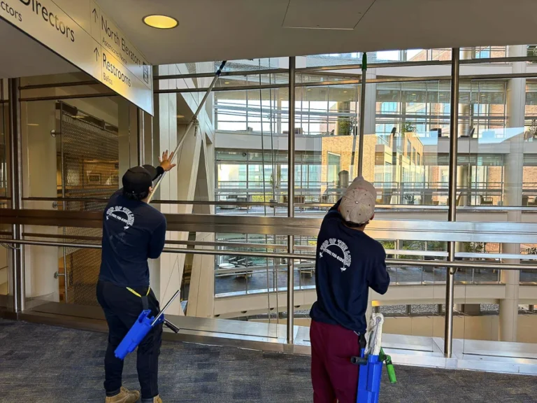 Two technicians cleaning interior atrium windows and glass railings