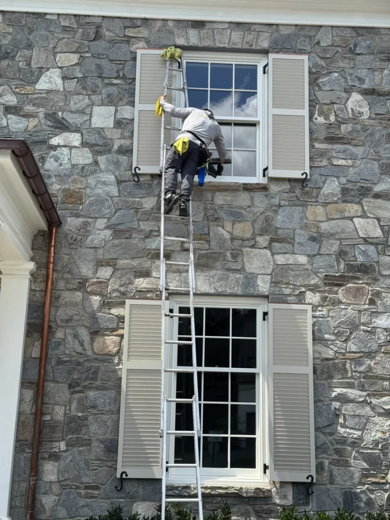 Top of the Line technician on a ladder cleaning a second-story window on a stone home
