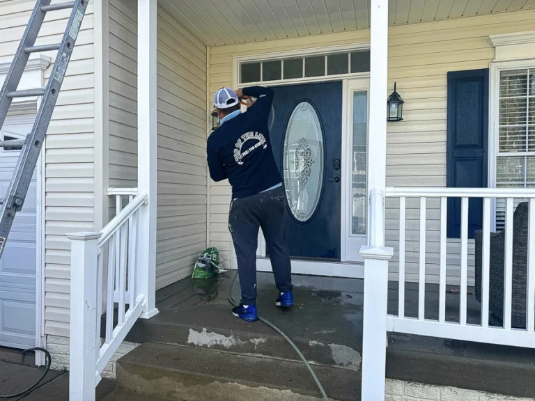 Technician cleaning the glass in a home's front door with a ladder nearby