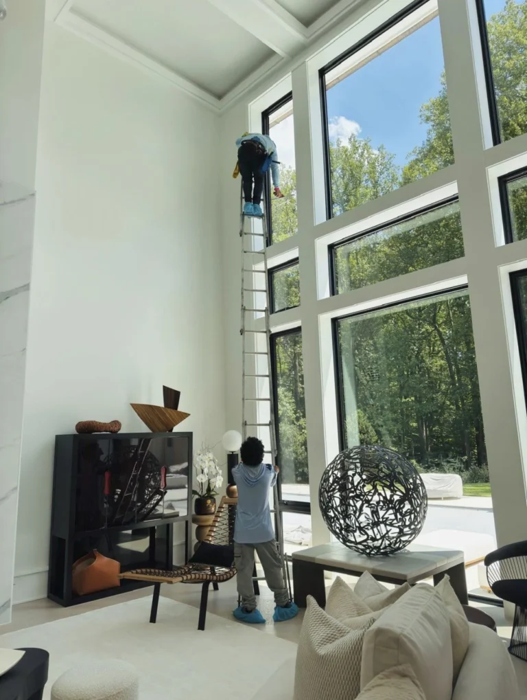 Two Top of the Line technicians cleaning tall interior windows in a home