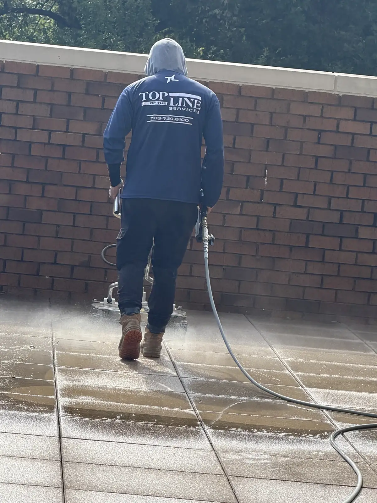 Top of the Line technician using a surface cleaner on an outdoor paved plaza.