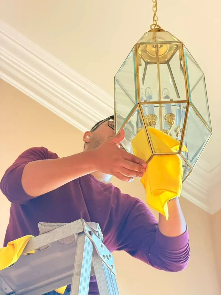 Technician wiping a hanging lantern-style light fixture by hand