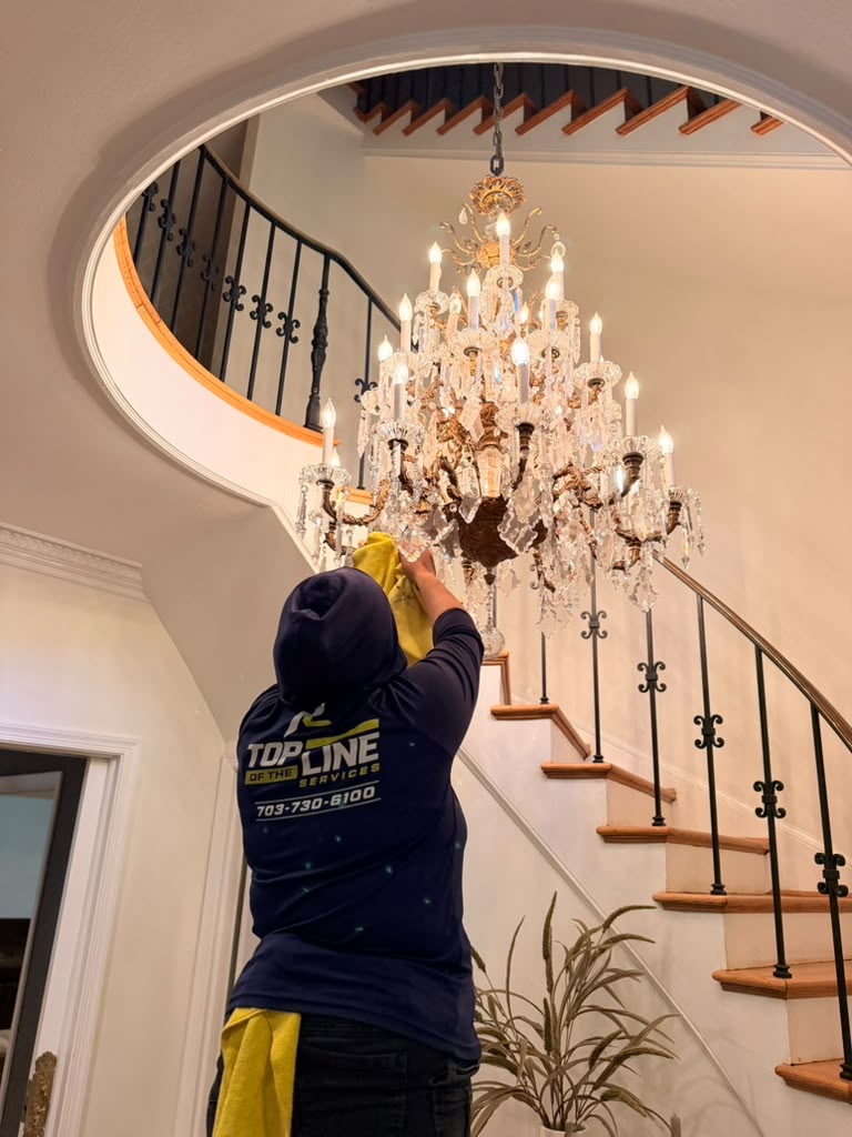 Top of the Line technician hand-cleaning a crystal chandelier in a residential foyer