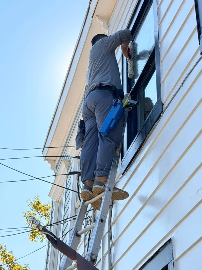 Technician cleaning a residential window from a ladder