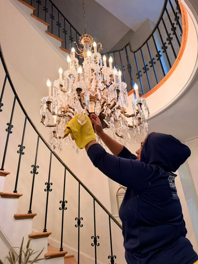 Technician using a yellow cloth to clean a crystal chandelier